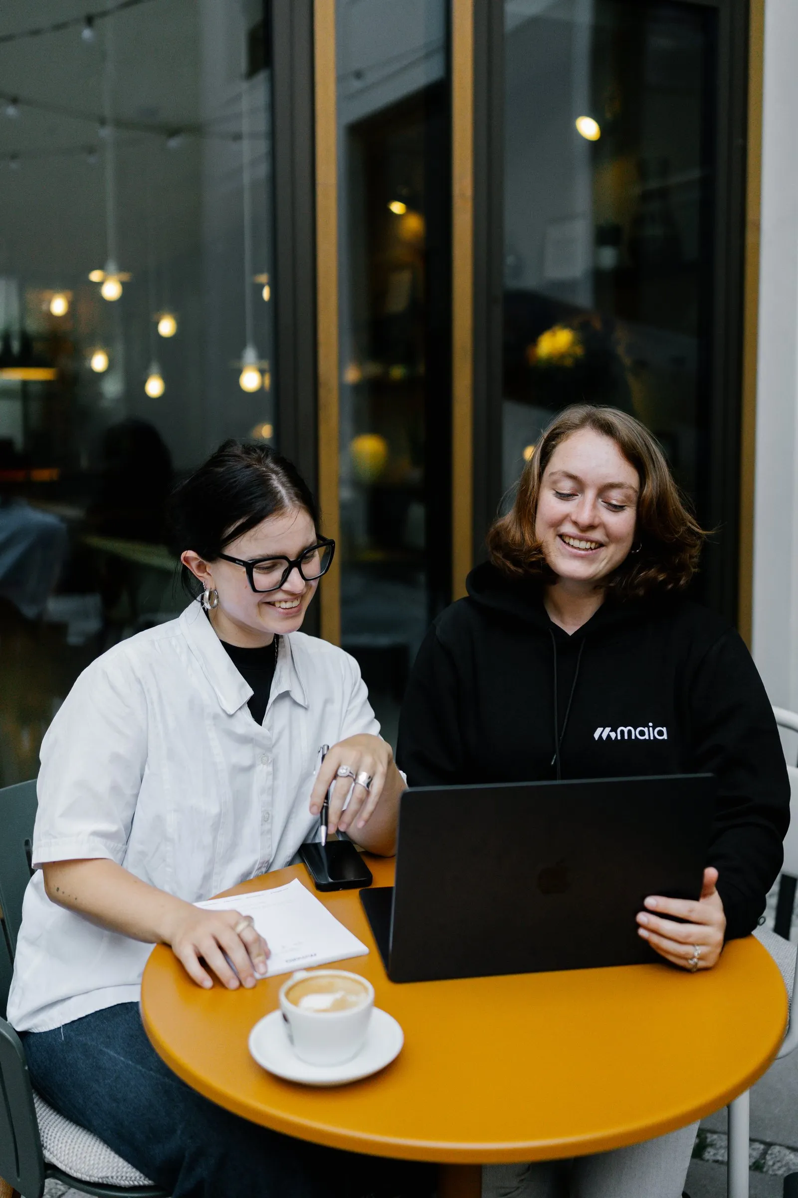 Two colleagues laughing together at a laptop in a café